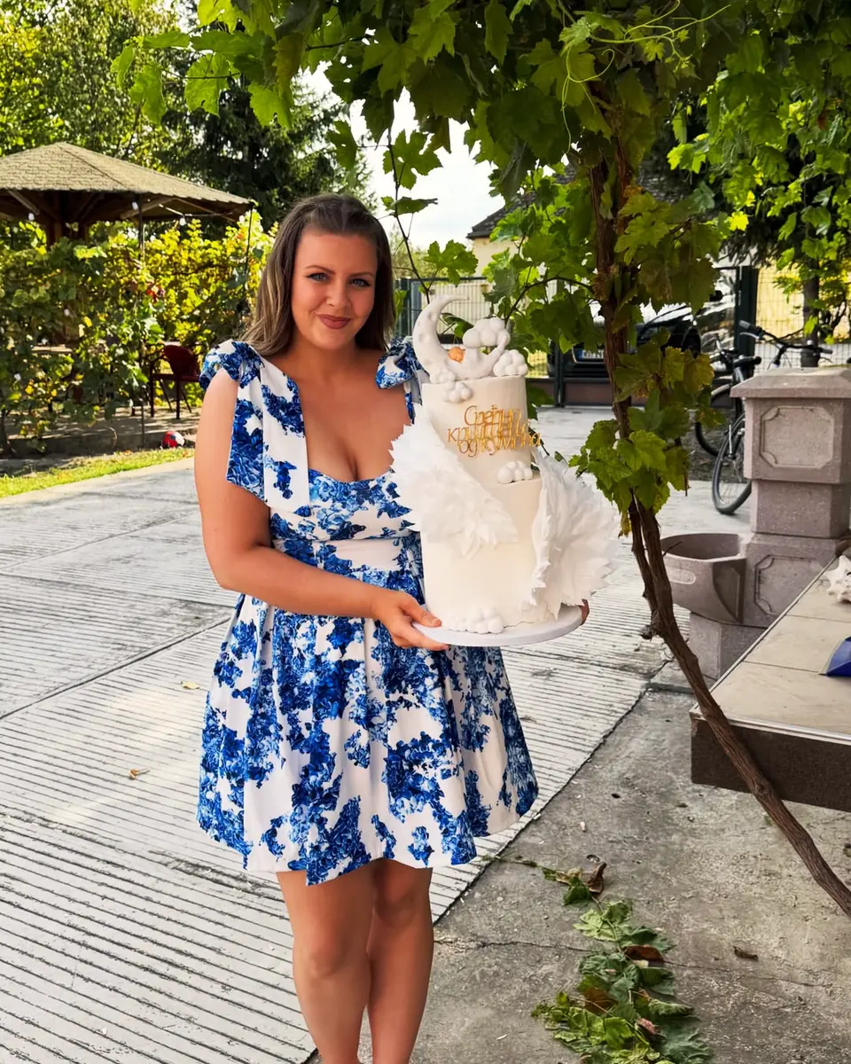 Jovana Panić drži belu tortu sa krilima, u bašti